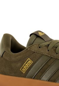 Olivengrüne Adidas-Sneaker aus Wildleder und Leder, mit goldener Markenpräsentation und drei Streifen, einer Gummisohle und einer strukturierten Zunge.