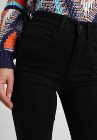 Jeans ajustados negros fabricados con una tela elástica, que presentan un diseño clásico de cinco bolsillos y una silueta ceñida.