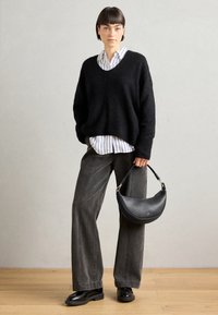 Pullover oversized preto e peludo combinado com uma camisa riscada em branco e azul, calças largas cinzas e uma bolsa de couro preta com sapatos pretos.