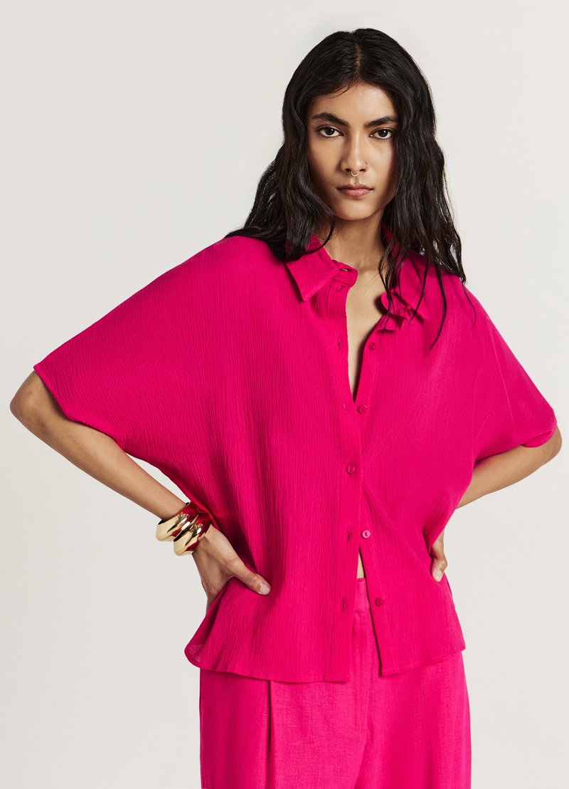 Chemise rose surdimensionnée à boutons, en tissu texturé, manches courtes et coupe décontractée. Remarquable pour sa couleur vibrante et son design décontracté.