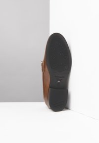 Braune Lederschuhe mit schwarzer Gummisohle und runden Profilen. Seitlicher Reißverschluss und Logodetail; schräg vor einem weißen Hintergrund.