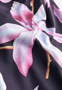 Kvetinová textília s veľkými ružovými a svetlomodrými vzormi orchideí na tmavom pozadí, s detailnou textúrou v okvetných lístkoch a listoch.