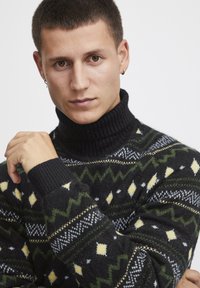 Pletena turtleneck pulover v črni barvi, okrašen z belimi, zelenimi in rumenimi geometrijskimi vzorci. Ribo nibna obroba in manšete, teksturirana tkanina.