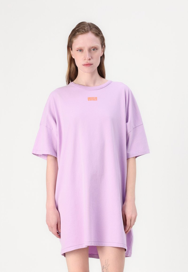 Per didelių size lilac spalvos t-shirt suknelė, pagaminta iš minkštos medvilnės, su apvaliu iškirpimu ir trumpomis rankovėmis, priekyje esantis mažas oranžinis logotipas.
