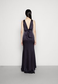 Lång, marinblå satin klänning med djup V-rygg och en knytning i midjan. Åtsittande silhuett som vidgar sig vid fållen för en jämn finish.