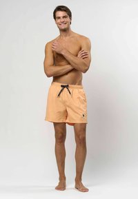 Perzik zwemshorts met een elastische tailleband, zwarte trekkoord en een klein logo-detail, met een lichte, soepele textuur.