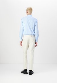Helles blaues Hemd mit Knöpfen, weiße Slim-Fit-Hose und schwarze Schuhe. Das Hemd hat lange Ärmel; die Hose hat Taschen auf der Rückseite und eine glatte Textur.