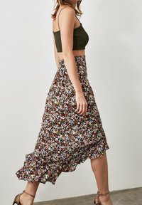 Floral midi skirt in dark fabric with ruffles, featuring multi-colored blooms. Paired with a fitted olive green top and strappy sandals.