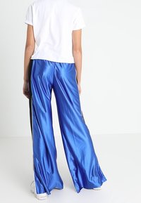 Pantalones anchos de satén azul con rayas laterales negras, que presentan una textura suave y un ajuste holgado, combinados con una camiseta de manga corta blanca.