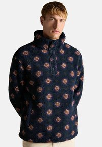 Fleece-Pullover mit hohem Kragen, mit marineblauem Grund und floralem Muster in Beige und Lila, versehen mit einem kurzen Reißverschluss.