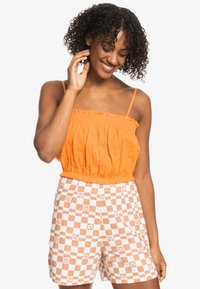 Orange cropped top med flæseudskæring parret med cremefarvede shorts med et orange ternet mønster og blomsteraccenter.