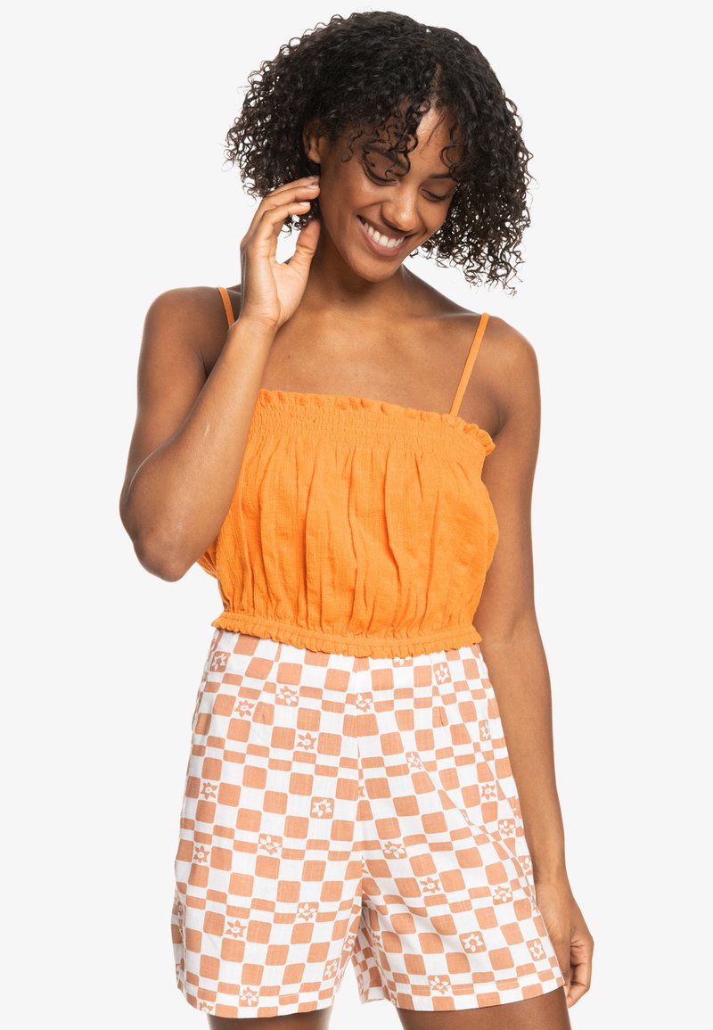 Oranje cropped top met een ruches neckline, gecombineerd met crèmekleurige shorts met een oranje geruit patroon en bloemenaccenten.