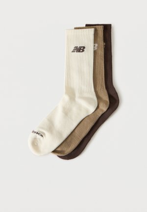 Tre ribbestrikkede crew-sokker i krem, beige og brun, hver med en liten New Balance-logo nær toppen.