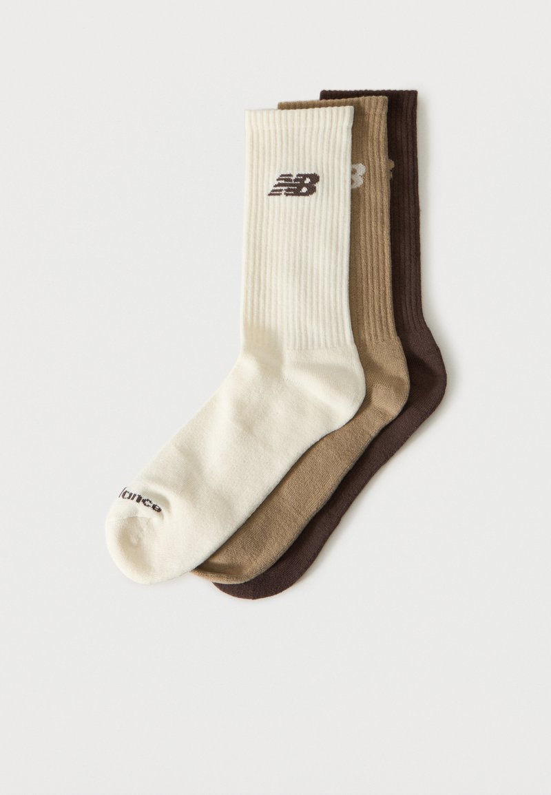 Tre ribbestrikkede crew-sokker i krem, beige og brun, hver med en liten New Balance-logo nær toppen.