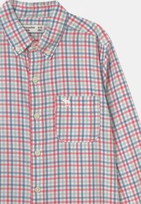 Koszula zapinana na guziki w wielokolorową kratkę w odcieniach czerwieni, niebieskiego i zieleni. Posiada kieszeń na piersi oraz lekką teksturę materiału.