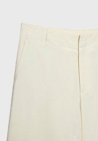 Pantalon ajusté de couleur crème avec une texture lisse, doté de poches avant et d'une coupe droite. Détails de couture subtils.