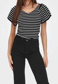 Musta-valkoraidallinen paita, jossa on röyhelöhihat, V-pääntie ja resoripintainen rakenne. Yhdistetty korkeavyötäröisiin mustiin housuihin, joissa on nappi.