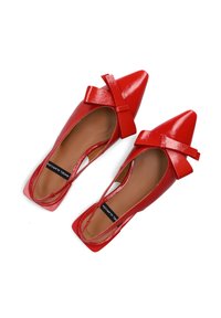 Rode gepatenteerde leren schoenen met een spitse neus. Heeft een strikaccent op één schoen en een open uitgesneden ontwerp. Tan kleurige zolen zichtbaar.