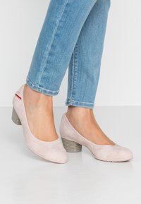 Světlé růžové kožené lodičky s kulatou špičkou, šitými detaily a texturovaným blokovým podpatkem. Nosené se světlými modrými džíny.