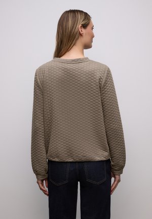 Khaki quiltet sweatshirt med lange ærmer, rund halsudskæring og en let cropped kant. Tekstureret mønster over det hele. Mørke denimbukser er synlige.