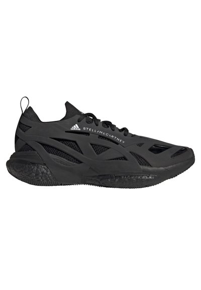 Sneaker de sport noir avec une tige en mesh, des superpositions géométriques audacieuses et une semelle en caoutchouc texturée. Il présente des lacets et un emblème sur le côté.