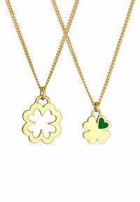 Goldene Halsketten mit floralen Anhängern; eine hat ein durchbrochenes Design, während die andere einen grünen Herzakzent aufweist. Kettenmuster.