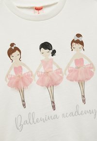 Valkoinen collegepaita, jossa on kolme ballerina-kuvasta. Ballerinat ovat pukeutuneet vaaleanpunaisiin tutuihin, joissa on tyllykerroksia; koristeellinen teksti lukee "Ballerina-akatemia."