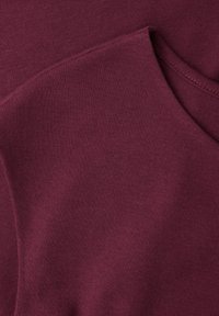 Gros plan sur un tissu bordeaux plié montrant les bords cousus et une texture douce et lisse.