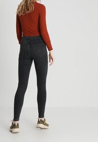 Jeans negros ajustados con cintura alta, de textura suave, con dos bolsillos traseros y un dobladillo sutil deshilachado en los tobillos.