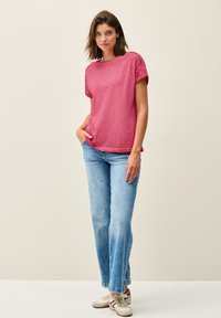 Short-sleeve, crew-neck, pink T-shirt in a relaxed fit, paired with light blue flared jeans and beige sneakers with maroon accents.