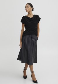 Blusa nera drappeggiata con maniche corte abbinata a una gonna nera alla caviglia con vita elasticizzata e texture liscia.