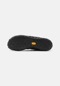 Semelle de chaussure en caoutchouc noir avec un motif d'adhérence ondulé texturé et une petite étiquette orange au centre.