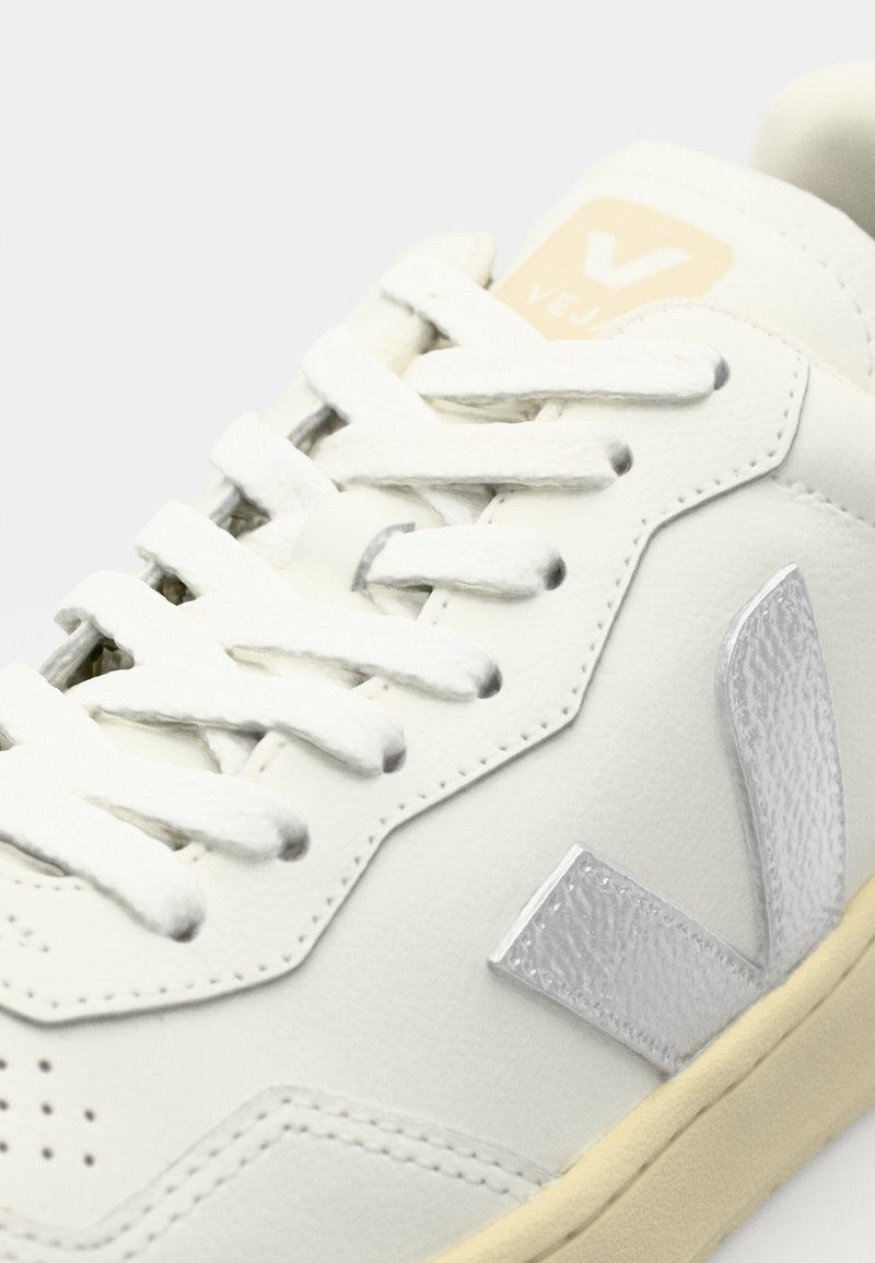 Baskets en cuir blanc avec des accents argentés, logo texturé, lacets plats blancs et design perforé sur le bout. Semelle en caoutchouc couleur crème.