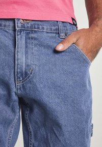 Mid-blå denimjeans har en rak skärning, fem fickor, synliga sömmar och en synlig logotag på midjebandet.