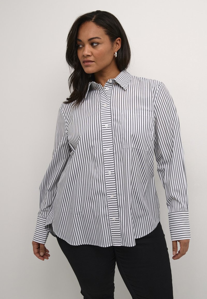 Chemise à rayures noire et blanche avec un col, des manches longues et une poche poitrine, dotée d'un ourlet arrondi.