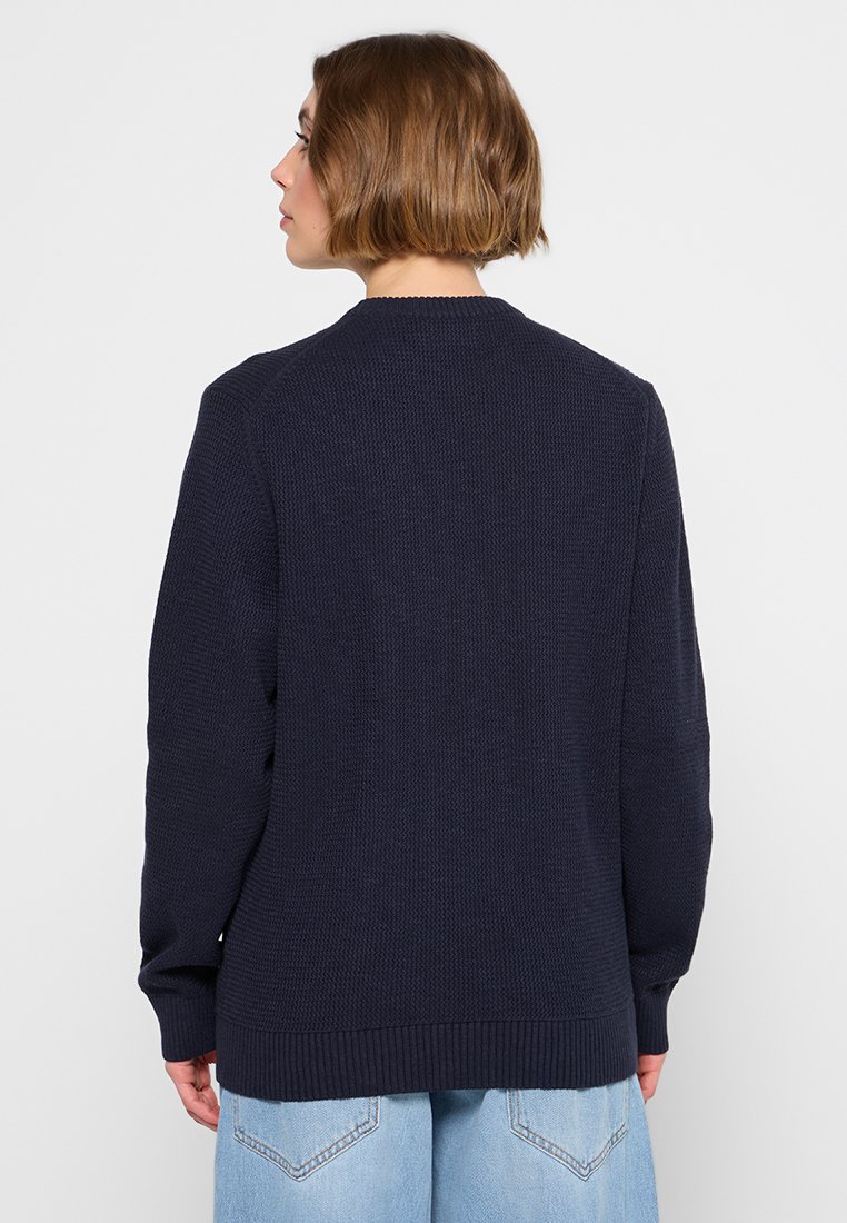 Granatowy sweter robiony na drutach z okrągłym dekoltem, ściągaczem u dołu i przy mankietach, ozdobiony teksturowanym wzorem oraz długimi rękawami. Widok z tyłu.