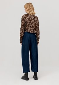 Bluzka w cętkowany wzór z długimi rękawami połączona z ciemnoniebieskimi spodniami w szerokim kroju i czarnymi botkami za kostkę. Gładkie tekstury, luźny fason.