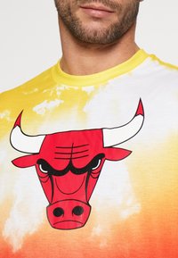 Koszulka z gradientowym wzorem kolorów od żółtego do pomarańczowego z dużym czerwonym wizerunkiem byka na przodzie. Mi�ękki bawełniany materiał, okrągły dekolt.