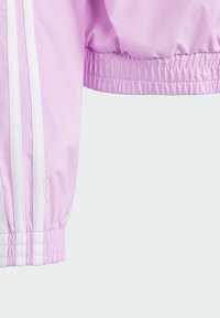 Svetle růžová rukávová část bundy s elastickými manžetami a bílými pruhy po stranách. Hladká, lesklá tkanina s nařasenou texturou na spodním lemu.