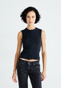 Débardeur côtelé marine sans manches avec un col rond, fermeture à boutons sur le devant et un design court. Associé à un jean en denim noir.
