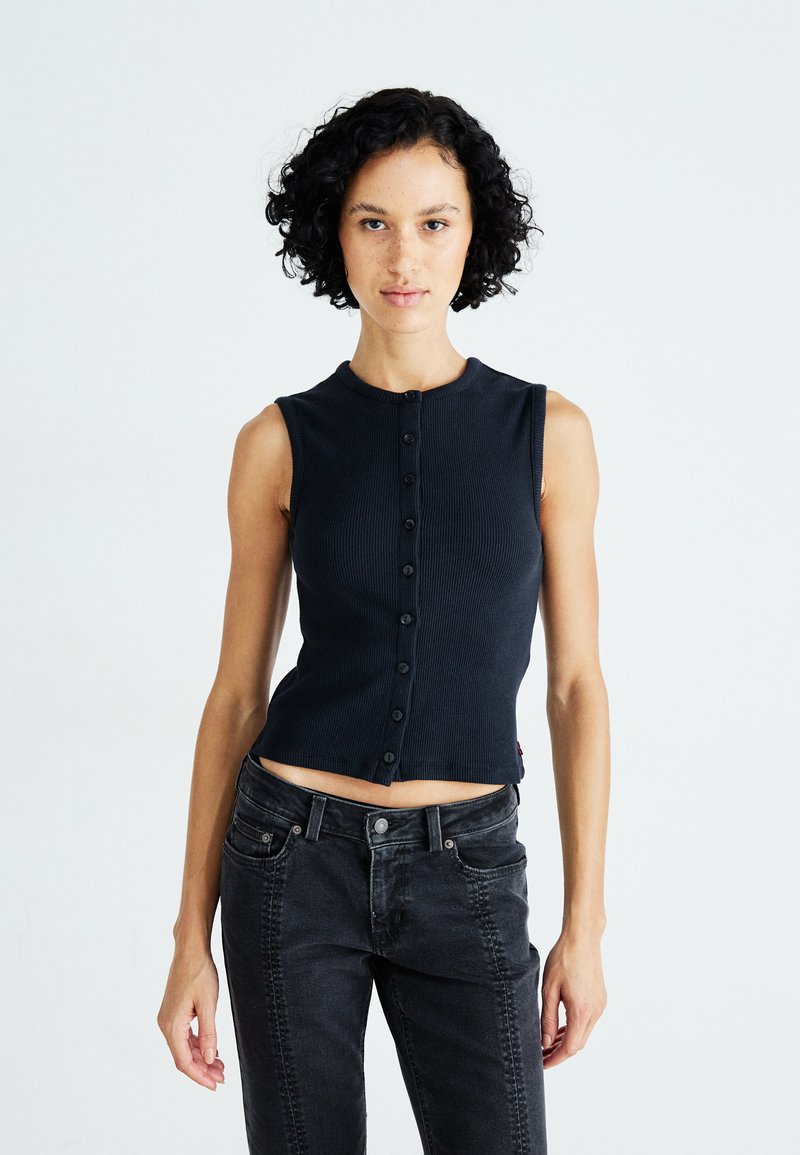 Débardeur côtelé marine sans manches avec un col rond, fermeture à boutons sur le devant et un design court. Associé à un jean en denim noir.