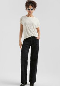 Haut blanc texturé à manches courtes et coupe décontractée, associé à un jean noir à jambes larges avec un motif zèbre subtil. Bottines noires.
