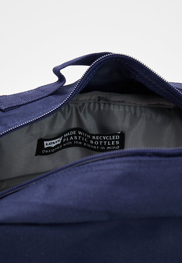 Vista interior de una bolsa azul marino que muestra una etiqueta que indica que está fabricada con botellas de plástico recicladas, diseñada pensando en el planeta.