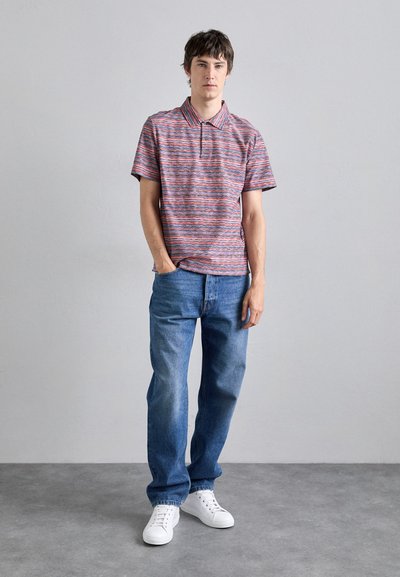 Cămașă polo cu dungi în roșu, albastru și alb; mâneci scurte și guler. Asortată cu blugi de denim bleu deschis și adidași albi.
