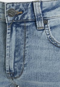 Calças de denim azul claro com um desbotado. As características incluem um fecho de botão metálico, costuras superiores e um design de cinco bolsos.