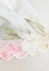 Blumige Mesh-Stoff mit Pastellfarben, gewelltem Rand und weicher Textur, die verschiedene Farbtöne von Pink und Grün durch das transparente Design zeigt.