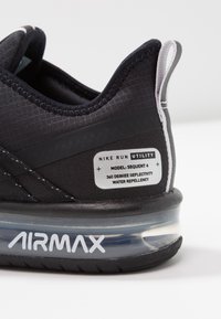 Czarny sneaker Nike Air Max z teksturowaną cholewką, odblaskowymi akcentami i przezroczystą podeszwą z poduszką powietrzną. Etykieta zawiera informacje o modelu i cechach.