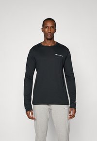 Black long-sleeve t-shirt made of soft fabric, featuring a crew neck, fitted design, and a small white logo on the left chest.