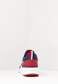 Vue arrière d'une chaussure de sport bleue et rouge, avec une tige en tissu texturé, un col rembourré et une semelle en caoutchouc blanche avec des accents rouges.