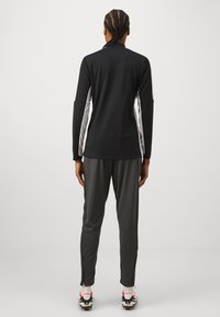 Zwart sportief langemouwen top met witte zijkanten, gecombineerd met donkergrijze tapered broek en sportieve schoenen met roze accenten.